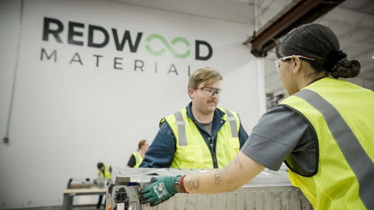 Two Redwood Materials employees hold an EV battery pack before it is disassembled.